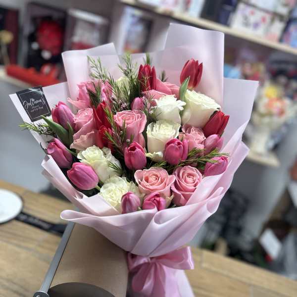 Pink and white rose bouquet with red tulips wrapped in pale pink paper