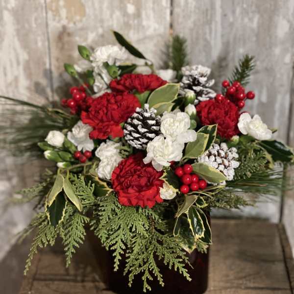 Red and white floral arrangement with pinecones in a dark container