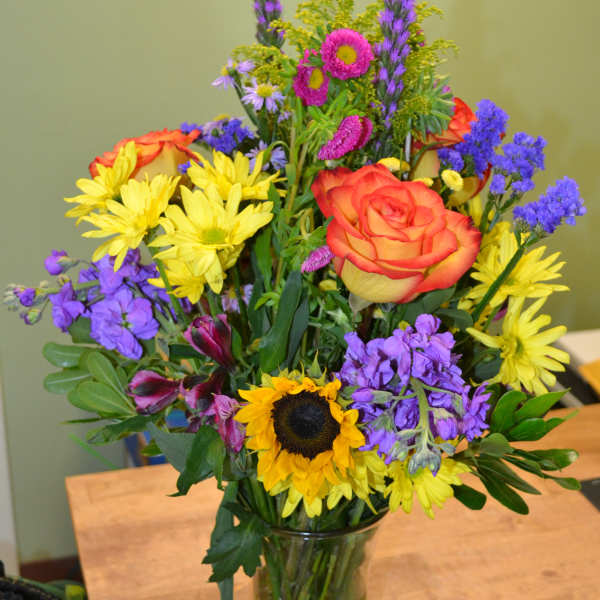 Colorful mixed bouquet in a clear glass vase with a sunflower and orange rose