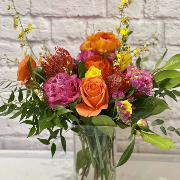 Mixed bouquet of orange, pink, and yellow flowers in a clear glass vase