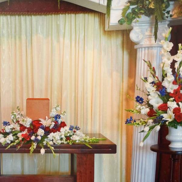 Symmetrical floral altar display with red, white, and blue flowers in white urns