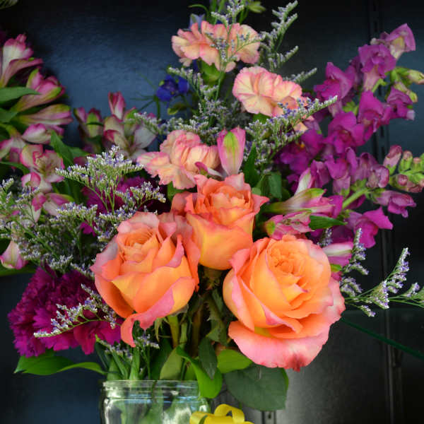 Orange roses and purple flowers in a glass vase with a yellow ribbon