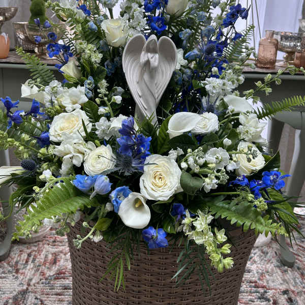 Tall blue and white flower arrangement with an angel figurine in a wicker basket