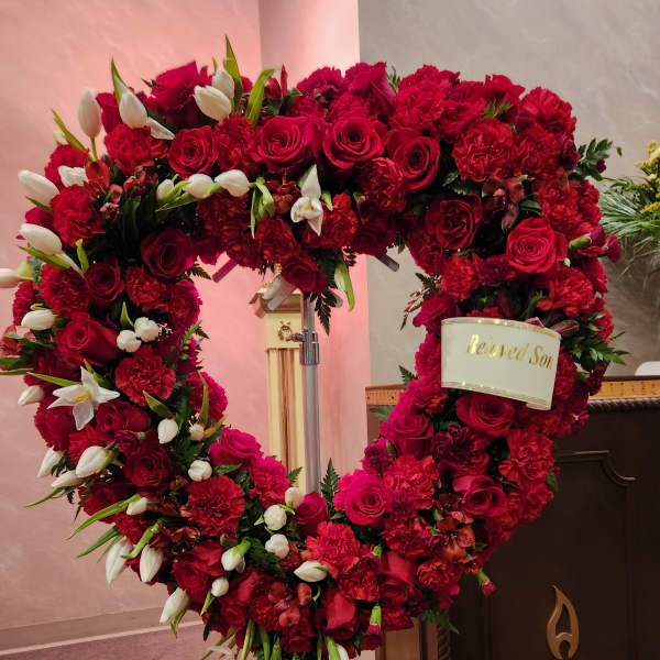 Heart-shaped red floral wreath with white tulips and a memorial ribbon
