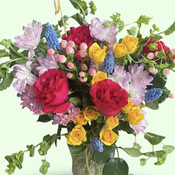 Mixed bouquet of roses, lavender blooms, and blue grape hyacinth in a glass vase