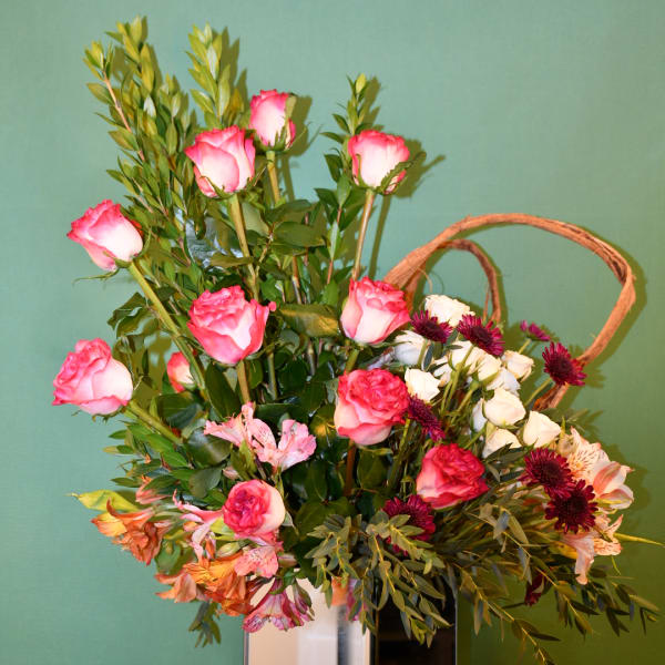 Pink roses and mixed flowers arranged in a white vase with a wicker handle