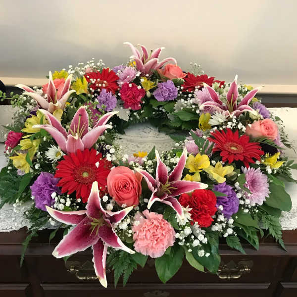 Circular floral wreath with pink lilies, red gerberas, and roses