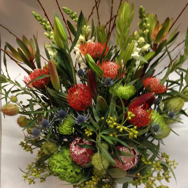 Tall mixed bouquet in a glass vase with red and green blooms