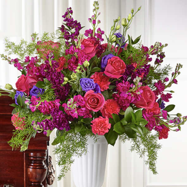 Tall pink and purple rose and carnation arrangement with trailing greenery in a white urn