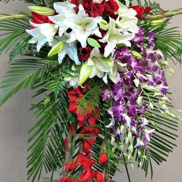 Tall standing floral spray with red roses, white lilies, and purple orchids
