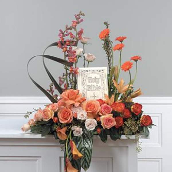Floral arrangement with peach and orange roses and tall orange blooms around a memorial card