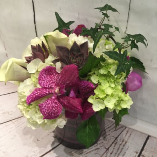 Low arrangement of white and green hydrangeas with bright pink orchids and calla lilies in a glass vase with trailing ivy