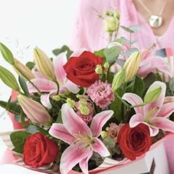 Bouquet of pink lilies and red roses held by a person in pink