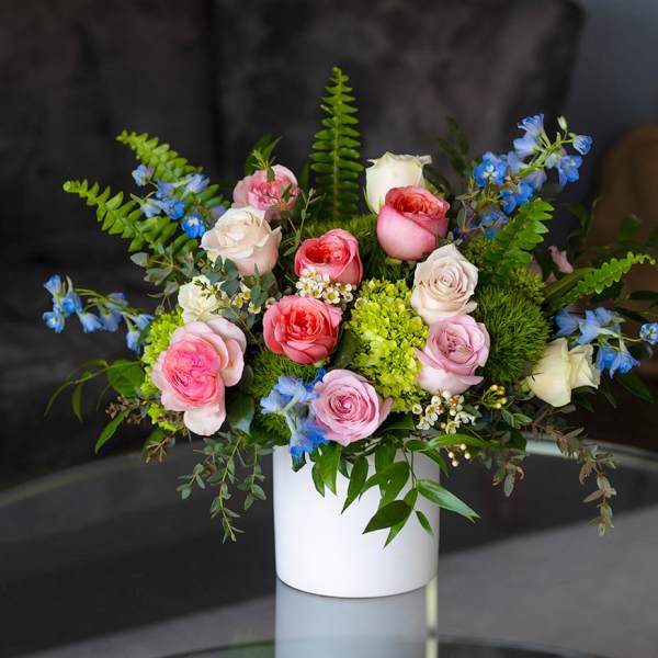 Arrangement of pink and cream roses with blue blooms in a white vase