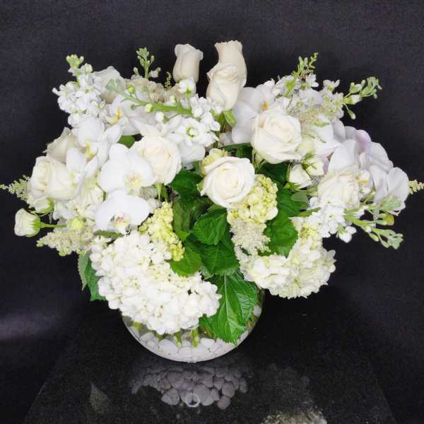 White roses and orchids arranged in a round glass vase