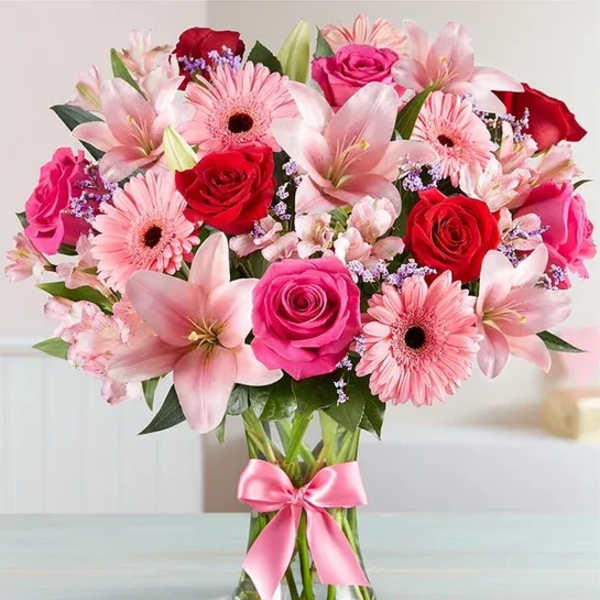 Pink and red mixed flower bouquet in a glass vase with a pink ribbon