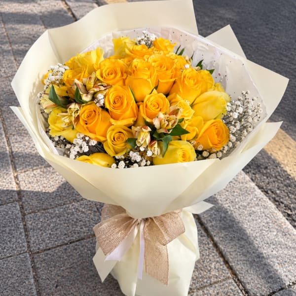 Bouquet of yellow roses wrapped in cream paper with a ribbon