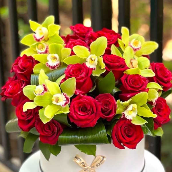 Red roses and lime orchids arranged in a white hat box