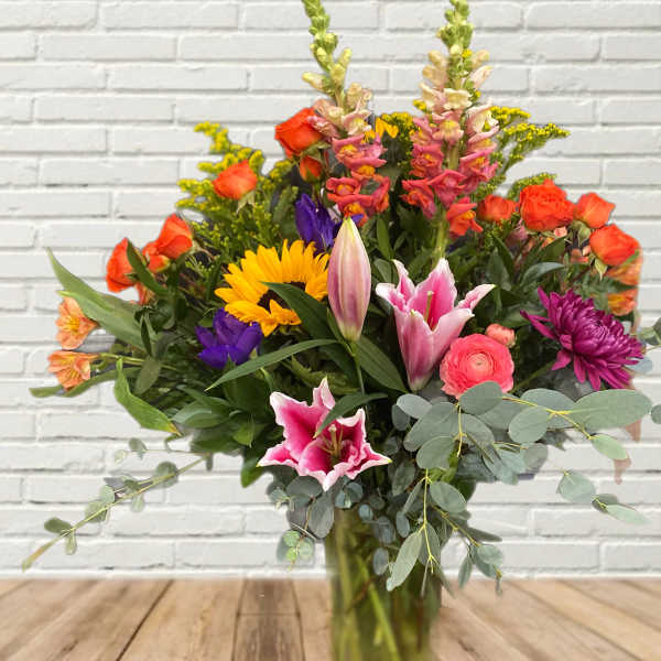 Colorful mixed bouquet in a glass vase with sunflowers, roses, lilies, and snapdragons