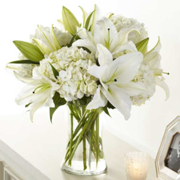 White lilies and hydrangeas arranged in a clear glass vase on a light-colored surface