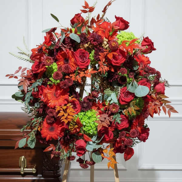 Large red floral wreath on a stand beside a casket