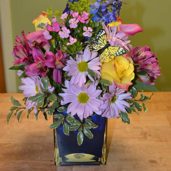 Colorful mixed bouquet in a blue glass vase with a butterfly decoration