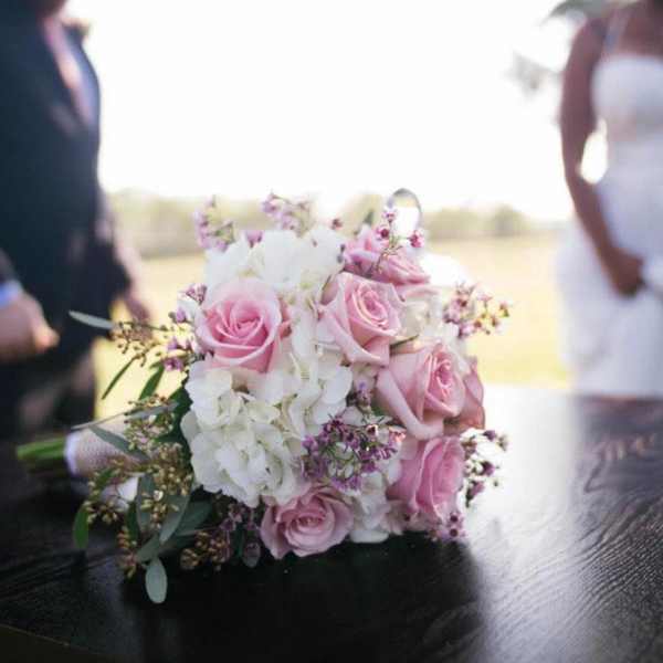 Pink and white bridal bouquet on a table with a bride and groom blurred in the background