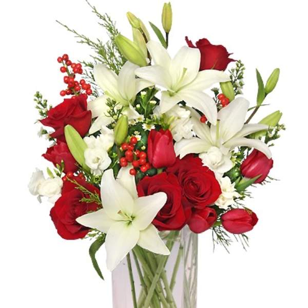 Tall clear vase with white lilies, red roses, and red berries in a mixed arrangement