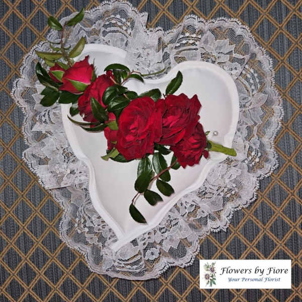 Red roses arranged in a white heart-shaped holder with lace trim