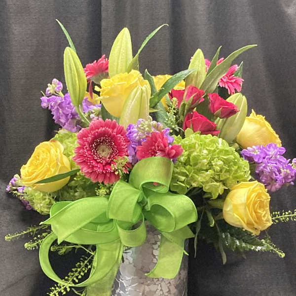 Colorful bouquet of roses, gerbera daisies, lilies, and hydrangeas in a silver vase
