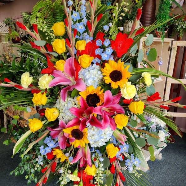 Large standing floral spray with sunflowers, pink lilies, and yellow roses