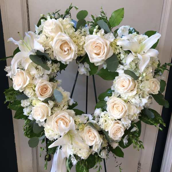 Heart-shaped floral wreath of white roses and lilies on a stand