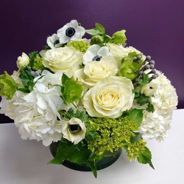 White roses and hydrangeas with green accents in a low vase arrangement