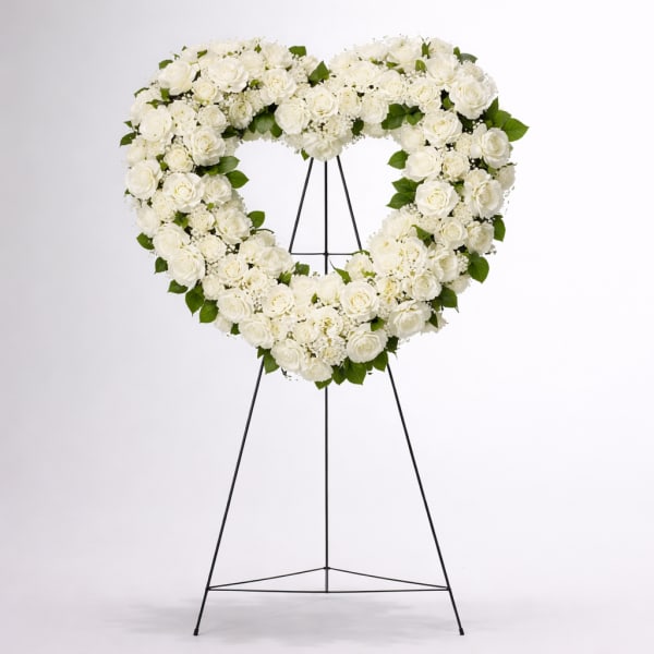 Heart-shaped white floral wreath on a black stand