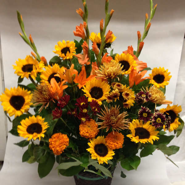 Mixed bouquet of sunflowers and orange flowers in a dark basket