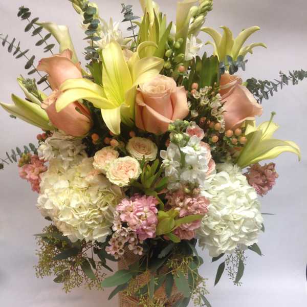 Bouquet of peach roses, yellow lilies, and white hydrangeas in a burlap-wrapped vase