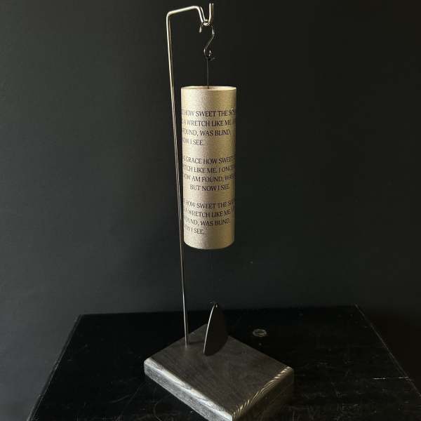 Gold wind chime hanging from a metal stand on a dark base