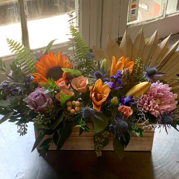 Mixed floral arrangement in a wooden box with sunflowers, roses, and lilies