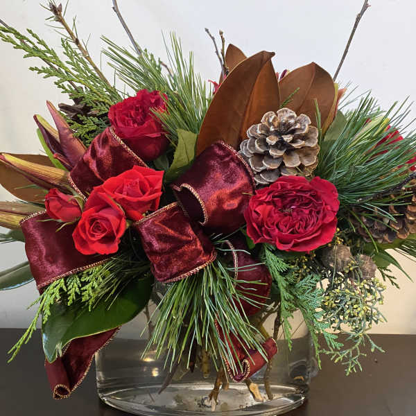 Red roses in a glass vase with burgundy ribbon and pinecones