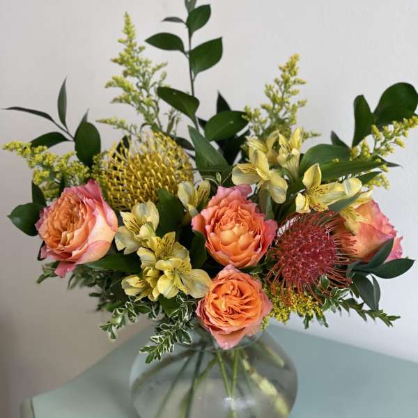 Bouquet of peach roses and yellow flowers in a round glass vase