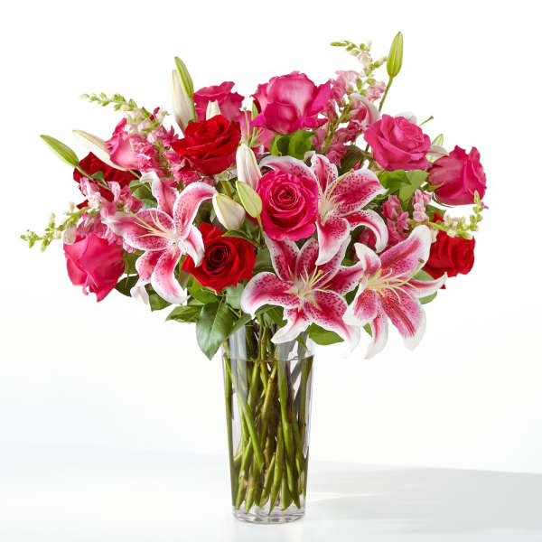 Pink and red roses with lilies in a clear glass vase