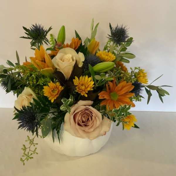 Mixed bouquet in a white pumpkin-shaped vase with cream roses and orange blooms
