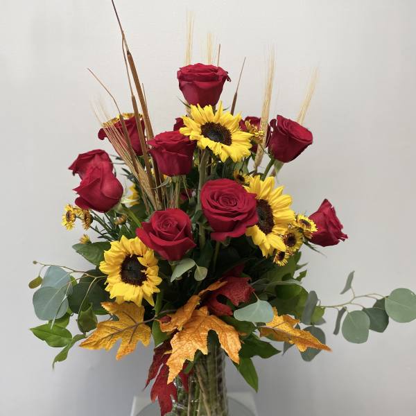 Red roses and yellow sunflowers in a clear glass vase