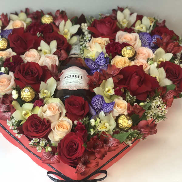Heart-shaped flower box with roses, orchids, and chocolates around a bottle of wine