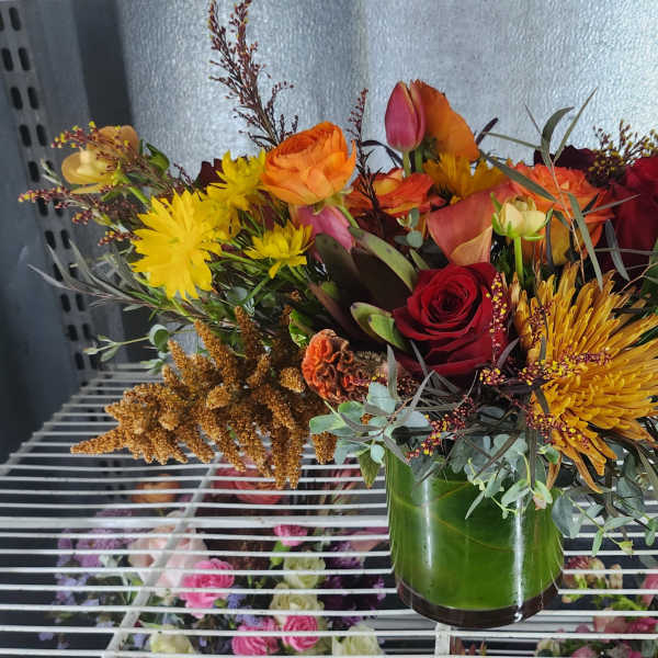 Mixed bouquet of red, orange, and yellow flowers in a green glass vase