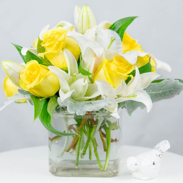 Yellow roses and white lilies in a clear glass vase