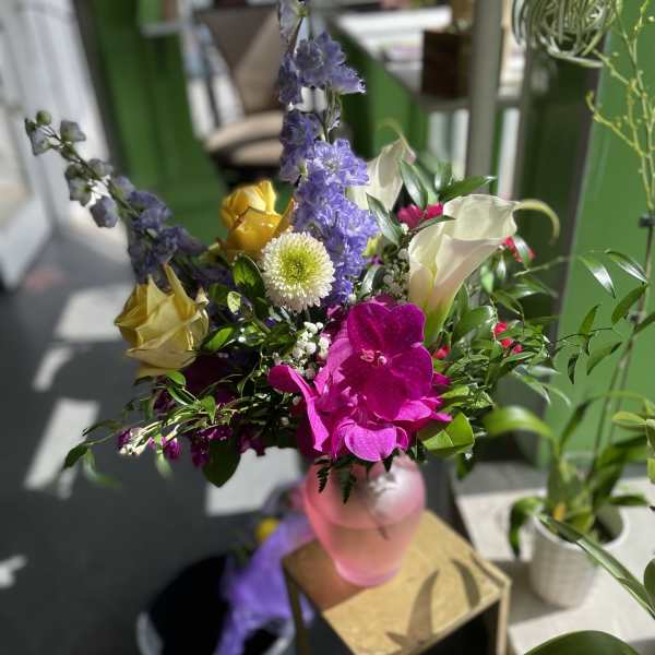 Mixed bouquet with purple, pink, yellow, and white flowers in a pink vase