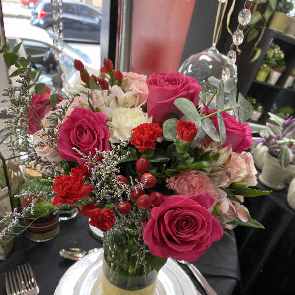Pink and red rose centerpiece in a glass vase on a set table
