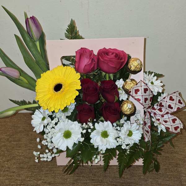 Bouquet of pink roses, a yellow gerbera daisy, and white daisies with chocolates and a ribbon