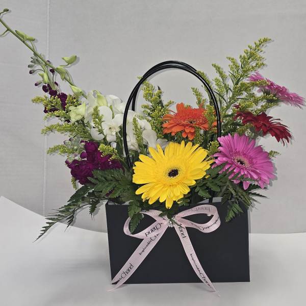 Mixed gerbera and orchid arrangement in a black gift bag with a pink ribbon